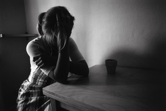 Female teenager sitting at table with head in hands --- Image by © Susanne Borges/A.B./Corbis