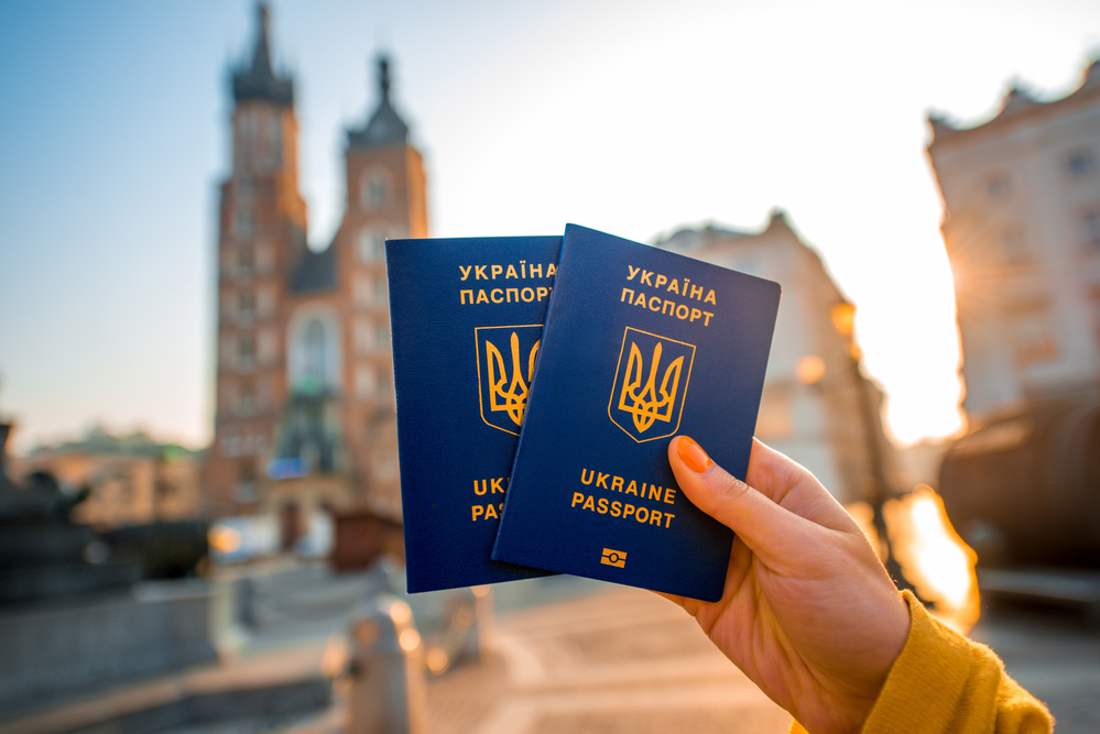 Female hands holding Ukrainian abroad passports on the Krakow city center background. Traveling to Europe from Post-Soviet countries or emigration to Europe concept